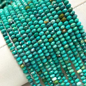 May include: Multiple strands of small, faceted turquoise beads arranged in parallel rows. The beads display a vibrant teal and green color palette with natural dark brown and black matrix inclusions, creating a textured, reflective surface.