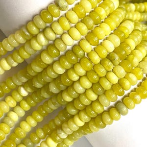 May include: Close-up of strands of yellow-green gemstone beads. The beads are a mix of light and darker shades of yellow-green, with a smooth, polished surface. The beads are strung together, creating a textured and colorful display.