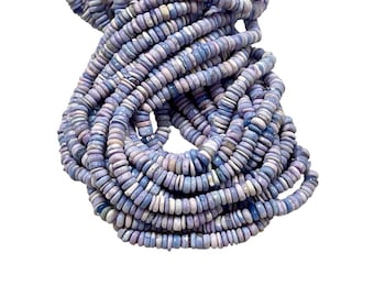 May include: A bundle of light blue and lavender gemstone beads. The beads are flat, round, and stacked together, creating a textured, layered effect. The beads are a mix of colors, with some appearing more blue and others more lavender.