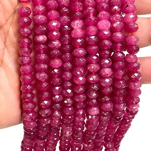 May include: Close-up of strands of faceted, deep pink gemstone beads. The beads are strung together, showcasing their polished, reflective surfaces. The beads are a vibrant shade of pink, perfect for jewelry making.