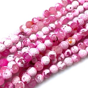 May include: A strand of pink and white agate beads with a speckled, textured surface. The beads are round and have a natural, organic look.