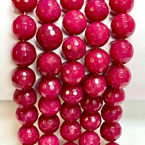 May include: Close-up of a strand of faceted, round, deep red beads. The beads are strung together, showcasing their polished, reflective surfaces. The beads are a vibrant shade of red, with a slightly translucent quality. The overall effect is one of elegance and sophistication.