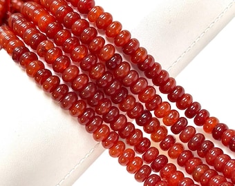 May include: A strand of red carnelian beads, each bead is round and slightly elongated, creating a textured look. The beads are strung together to form a long necklace or bracelet.