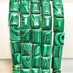 Può includere: Una collana di perline di malachite verde, ogni perlina è di forma rettangolare con una finitura liscia e lucida. Le perline hanno un motivo naturale a marmo.