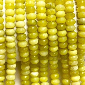 May include: Close-up of strands of yellow-green gemstone beads. The beads are round with a slightly flattened shape, and they have a smooth, polished surface. The color varies slightly, creating a subtle gradient effect. These beads are suitable for jewelry making.