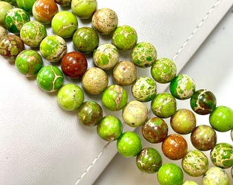 Puede incluir: Una hebra de cuentas de jaspe verde, marrón y blanco. Las cuentas son redondas y tienen un patrón moteado.