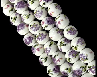Può includere: Una collana di perline in ceramica bianca con un motivo floreale viola. Le perline sono rotonde e hanno una finitura lucida.