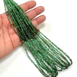 May include: A strand of green emerald chip beads. The beads are small and irregular in shape. The strand is long and is shown in a hand.
