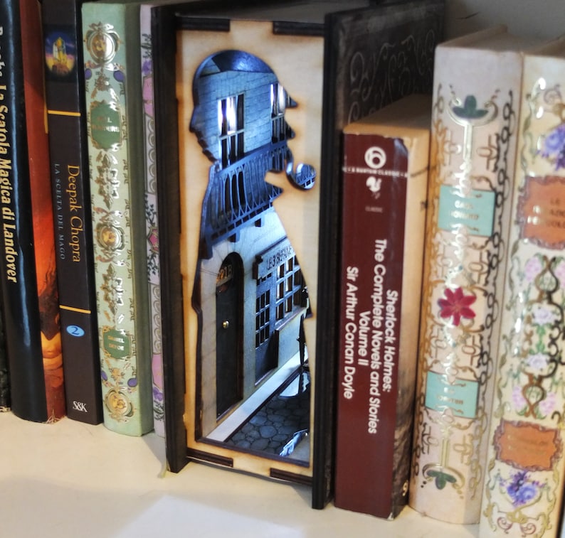 Pode incluir: Um separador de livros de madeira com uma silhueta de Sherlock Holmes em p&eacute; em frente a um edif&iacute;cio. O separador de livros &eacute; iluminado por tr&aacute;s, criando um brilho quente. O separador de livros est&aacute; colocado entre duas estantes, com livros de ambos os lados.