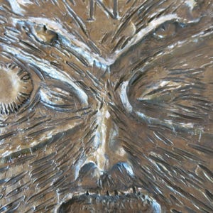 Puede incluir: Primer plano de una superficie de madera texturizada, marr&oacute;n, con una cara tallada. La cara tiene ojos hundidos, una nariz prominente y el ce&ntilde;o fruncido.