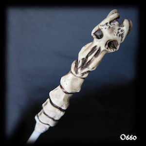 May include: A white bone-like wand with a skull-shaped top. The wand is made of a smooth, textured material and has a slightly curved shape.