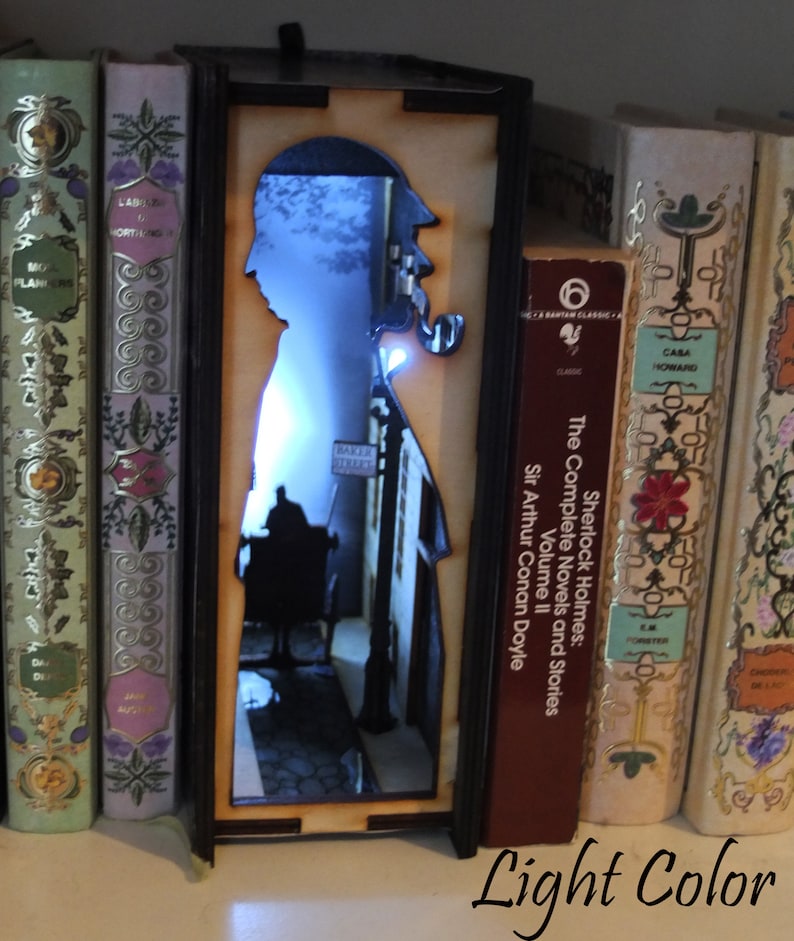 Pode incluir: Uma luz noturna de madeira em forma de livro com uma silhueta de Sherlock Holmes e uma cena de rua. A luz &eacute; iluminada com uma luz branca.