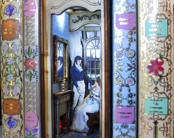 May include: A miniature diorama scene inside a book-shaped box. The scene depicts a man and woman in a room with a fireplace and a window. The box is surrounded by book spines with gold lettering.