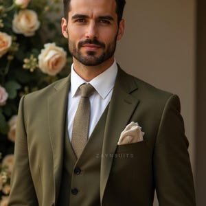 May include: Olive green three-piece suit with a white dress shirt and patterned tie. A pocket square is visible in the breast pocket. The suit is tailored and features the text "ZAYN TAILOR-MADE SUITS".