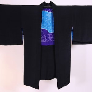 May include: A black Japanese kimono with a blue and purple patterned lining. The kimono is hanging on a hanger.
