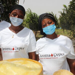 Three African Women in the forest of Ghana with face masks wearing an Aroma Depot White t-shirt in front of wooden bowls filled with yellow African Shea Butter.