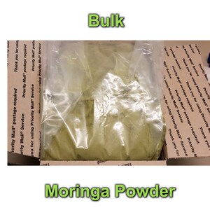 May include: A clear plastic bag filled with a large amount of green moringa powder. The bag is sitting inside a brown cardboard box with Priority Mail postage labels.