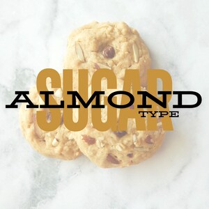 May include: Three almond sugar cookies, with a light brown color and visible almond pieces, stacked on top of each other. The cookies are on a white marble surface. The text "ALMOND SUGAR TYPE" is superimposed on the image.