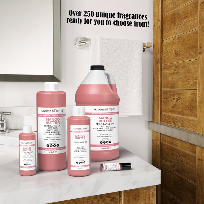 May include: Four bottles of Mango Butter Fragrance Oil in various sizes, from a small 10 ml bottle to a large 1 gallon bottle. The bottles are pink and have a white label with the text "Aroma Depot" and "Mango Butter Fragrance Oil" on them. The bottles are on a white countertop with a white towel hanging on a towel rack in the background.