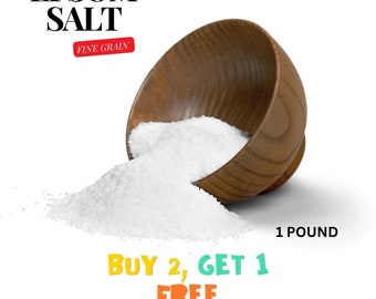 May include: A wooden bowl filled with white Epsom salt, spilling out onto a white background. The bowl is tilted to the side, and the salt is cascading out of it. The text "EPSOM SALT FINE GRAIN" is at the top of the image, and the text "1 POUND BUY 2, GET 1 FREE READ DESCRIPTION" is at the bottom of the image.
