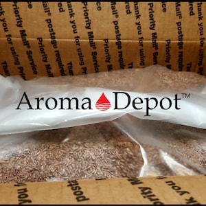 May include: A brown cardboard box with the text "Priority Mail Service" printed on it. The box is open and contains a clear plastic bag filled with brown seeds. The bag has the text "Aroma Depot" printed on it.