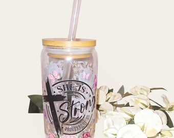 May include: A clear glass tumbler with a gold lid and a straw. The tumbler has a floral design with butterflies and the text "She is Strong Proverbs 31:25".