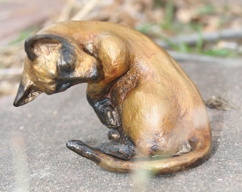 Könnte beinhalten: Eine kleine, bronzefarbene Figur eines Katzen, das sich in Schlafposition zusammengerollt hat. Das Fell der Katze ist detailliert mit einer strukturierten Oberfläche und die Augen sind geschlossen.