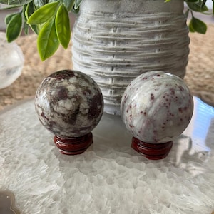 May include: Two red and white speckled crystal spheres on wooden stands. The spheres are about 2 inches in diameter.