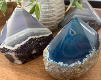 May include: Three agate crystal points, one blue, one purple, and one white, with a natural, rough exterior and a polished, smooth interior.