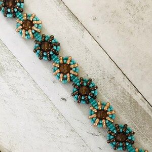 May include: A turquoise and brown beaded bracelet with a metal clasp and a decorative metal pendant. The bracelet features a repeating pattern of flower-shaped beads.