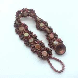 May include: A beaded bracelet with a brown button closure. The bracelet is made with red, brown, and beige beads in a flower pattern.