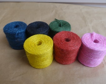 May include: Six spools of twine in different colors: blue, black, green, red, yellow, and pink. The spools are arranged in a circle on a brown surface.
