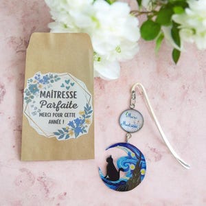 Peut inclure: Un marque-page en métal argenté avec une breloque ronde portant le texte Merci Maîtresse et un pendentif en forme de croissant de lune illustrant une silhouette de chat noir sur un ciel étoilé bleu, avec une enveloppe en papier kraft.