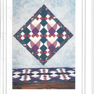 May include: A quilt pattern called "Angels and Four Patches" designed by Joanne M. Winn of Canada Goose Designs. The quilt features a diamond-shaped design with a white background and red, purple, and teal squares. The quilt is displayed on a wooden table with a matching runner.
