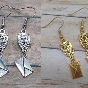 May include: Two pairs of owl-themed dangle earrings. One pair is silver-toned, the other gold-toned. Each earring features an owl charm and a small envelope charm. The earrings hang from a simple hook.