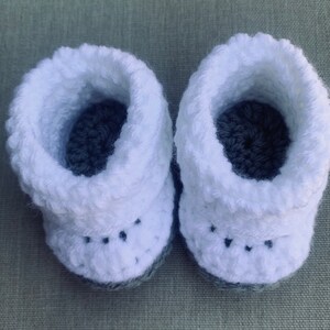 Op de afbeelding: Een paar witte gehaakte babyschoentjes met grijze gehaakte zolen.