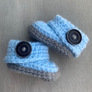 Op de afbeelding: Een paar babyschoentjes in lichtblauw met grijze randjes en zwarte knopen.