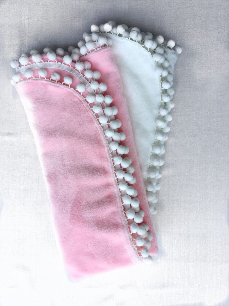 Op de afbeelding: Twee zachte dekens met witte pomponrand. Een deken is roze en de andere is wit.