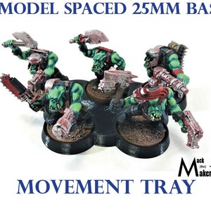 May include: Five green and red painted miniature figures on a black plastic movement tray. The tray is designed to hold 25mm bases and is spaced for five models. The tray is labeled "Movement Tray".