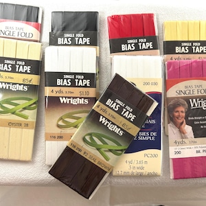 May include: Assortment of single fold bias tape in various colors, including white, brown, yellow, red, and pink. Each spool is labeled "Wrights" and includes the length in yards and meters. The tape is 1/2 inch wide.
