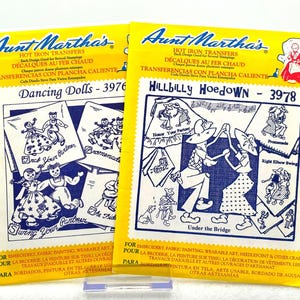 May include: Two yellow Aunt Martha's hot iron transfer packets featuring blue line art illustrations. The left packet is titled Dancing Dolls 3976, and the right packet is titled Hillbilly Hoedown 3978, both displaying various figures dancing.