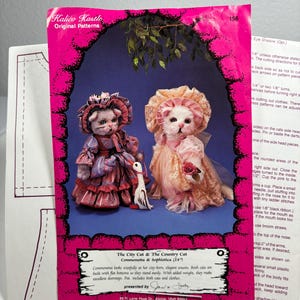 May include: A sewing pattern for two 24-inch dolls, a city cat and a country cat. The pattern includes instructions for making the dolls' clothes and accessories. The pattern is presented by Jaw and is from Kalico Kastle Original Patterns.