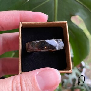 May include: A black and gold ring with a textured surface, displayed in a brown box.
