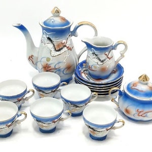 May include: A vintage porcelain tea set with a blue and white design, featuring a teapot, creamer, sugar bowl, saucers, and six teacups. The set has gold accents and a dragon motif. The teapot is approximately 8 inches tall.