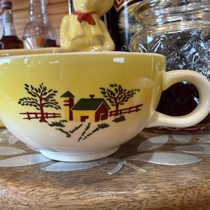 Peut inclure: Une tasse en céramique jaune et blanche ornée d'une illustration graphique représentant une ferme avec une grange, un silo, des arbres et une clôture. La tasse présente un corps arrondi, une large ouverture et une anse incurvée sur le côté droit.