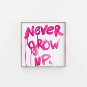 Puede incluir: Una impresi&oacute;n enmarcada con las palabras "NEVER GROW UP" escritas en pintura acuarela rosa. La pintura gotea por la p&aacute;gina, creando un efecto l&uacute;dico y fantasioso.