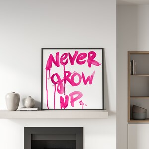 Puede incluir: Una impresi&oacute;n enmarcada con las palabras "NEVER GROW UP" escritas en pintura acuarela rosa. Las palabras gotean por la p&aacute;gina, creando un efecto l&uacute;dico y caprichoso.
