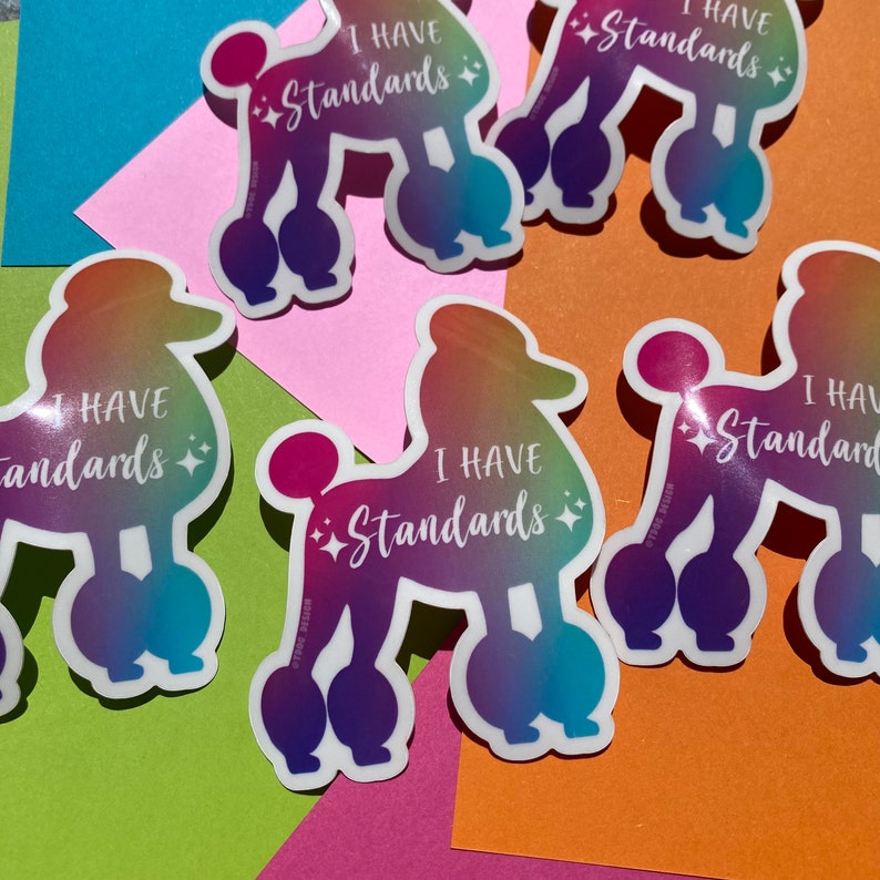 May include: Four iridescent rainbow stickers with a white poodle silhouette and the text "I have standards" in white. The stickers are on a variety of colored surfaces.