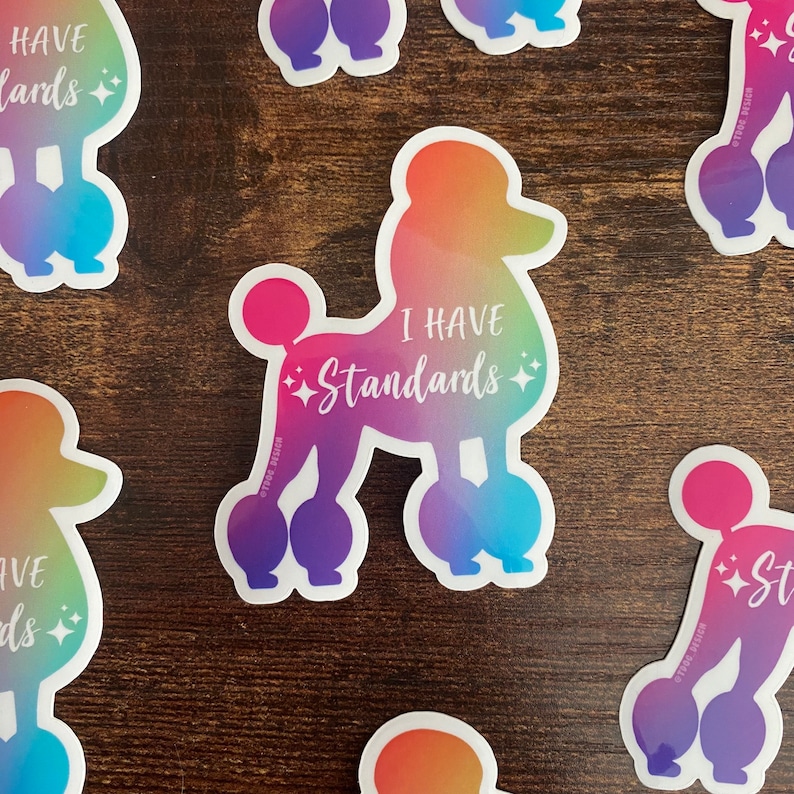 May include: A rainbow gradient sticker of a poodle with the text "I have standards" in white. The sticker is on a wooden surface.