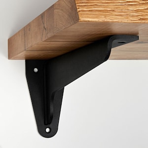 Op de afbeelding: Zwarte metalen plankensteun met een gebogen ontwerp. De steun is bevestigd aan een houten plank.